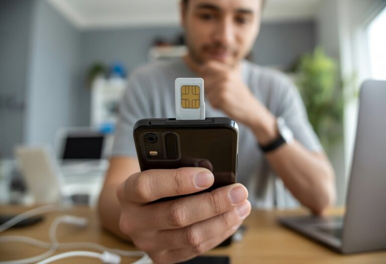 Pessoa segurando um smartphone com o compartimento do chip parcialmente aberto, olhando para a tela do aparelho em um ambiente interno moderno.